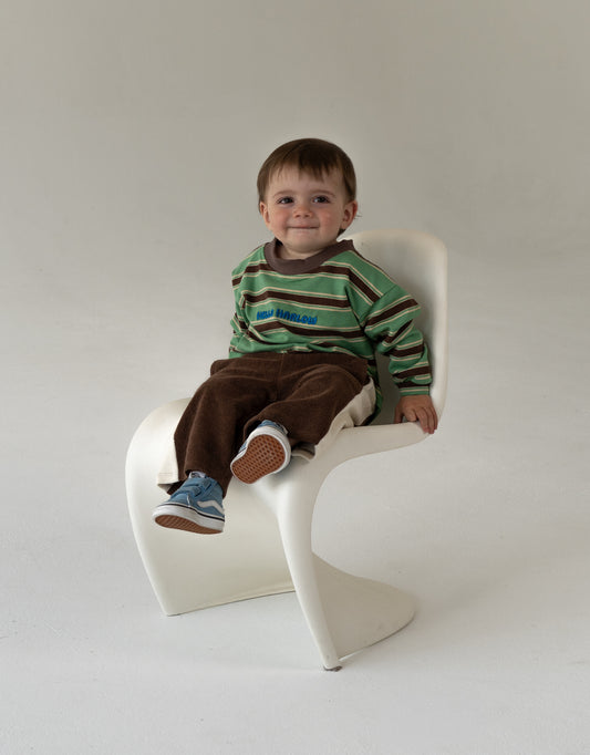 baby sitting on a white chair wearing a striped sweater and brown pants.