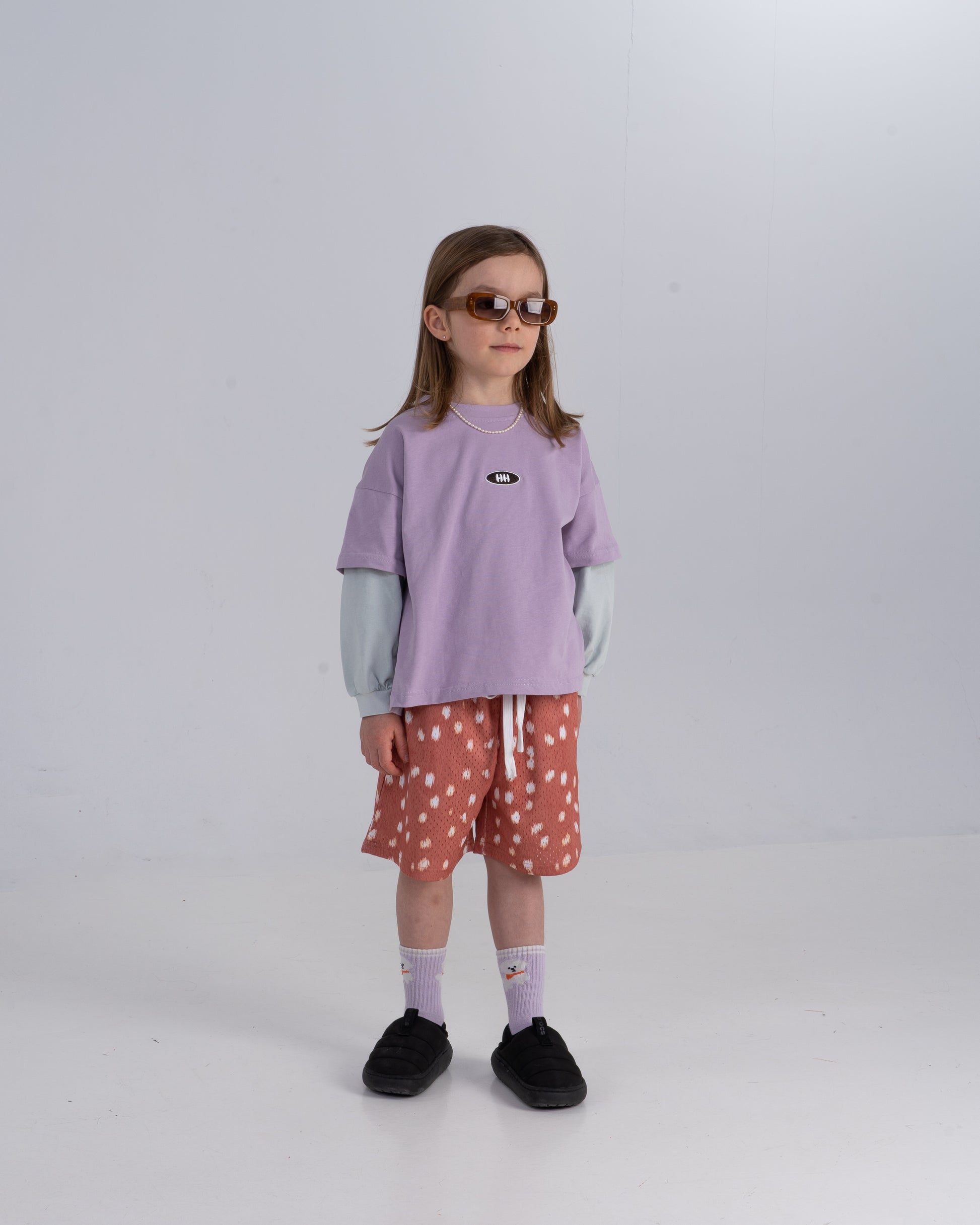 Child wearing a purple shirt and polka dot shorts on a white background