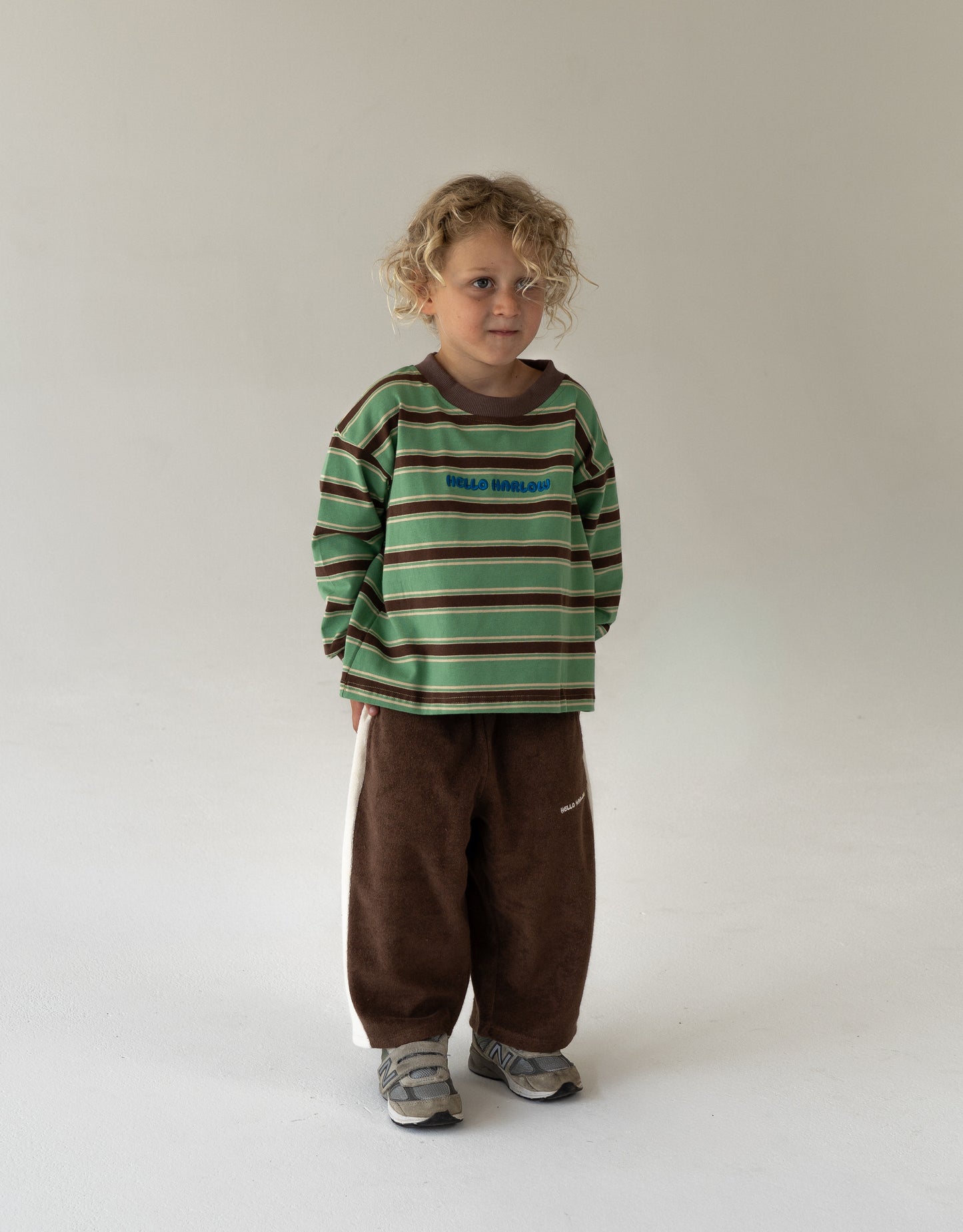 Child wearing a green and brown striped shirt with brown pants on a white background