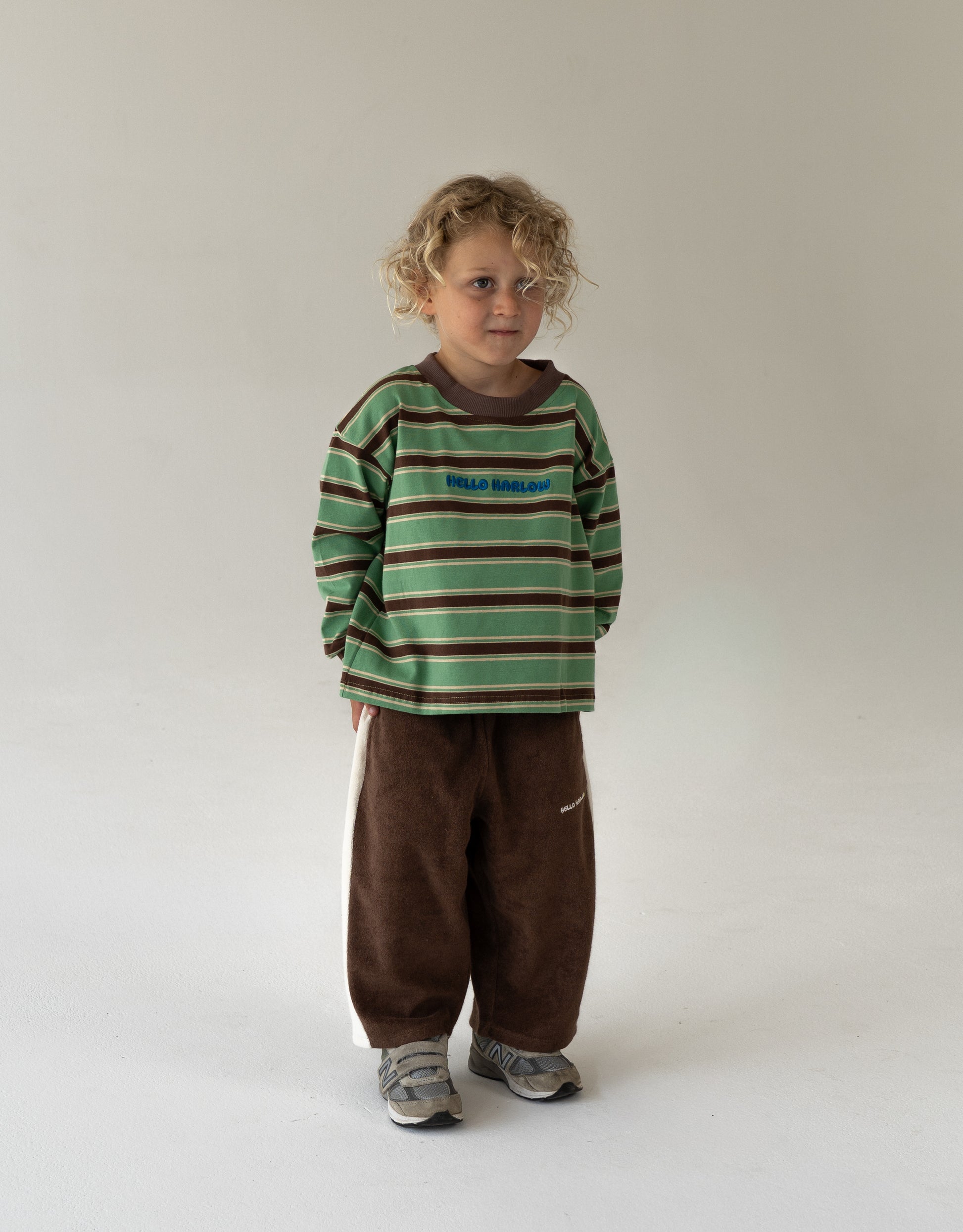 Child wearing a green and brown striped shirt with brown pants on a white background
