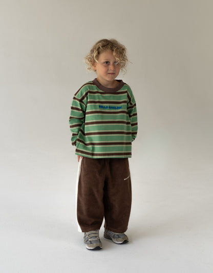 Child wearing a green and brown striped shirt with brown pants on a white background