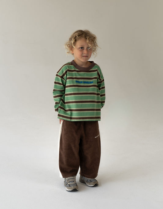 Child wearing a green and brown striped shirt with brown pants on a white background