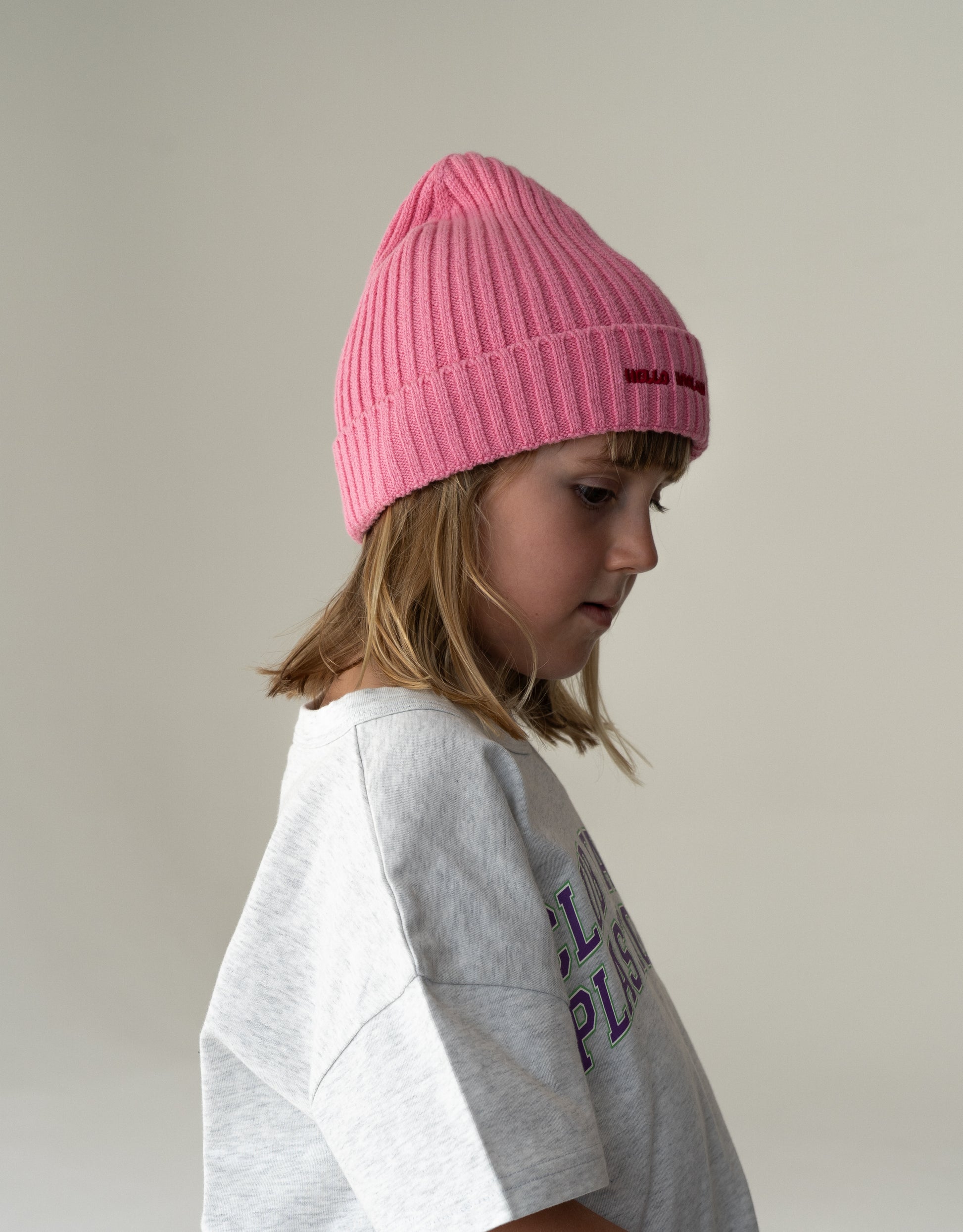 Child wearing a pink beanie and gray t-shirt with text on a plain background