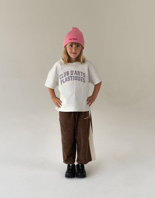 Child wearing cotton terry brown pants, pink cotton hat and an oversized t-shirt