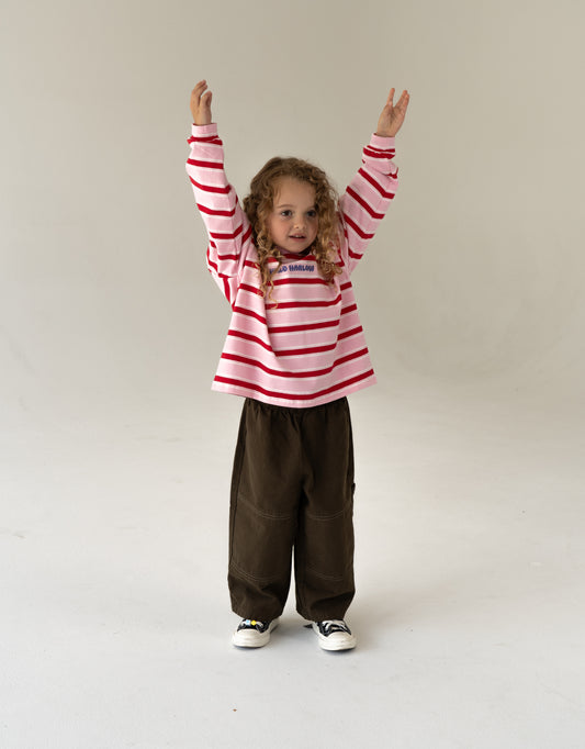 Child wearing a red and white striped shirt and brown pants on a plain background, oversized kids clothing 