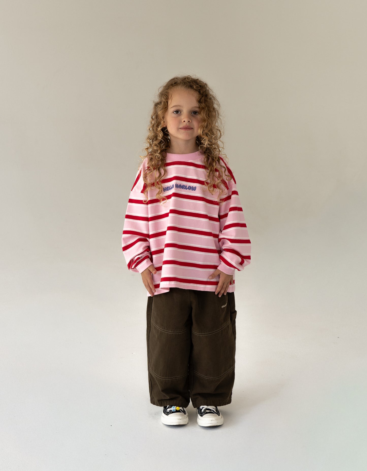 Child wearing a pink and red striped sweater with text, standing against a plain background